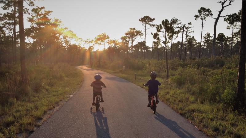 A view of two people walking down the trail with the sun setting in the background.